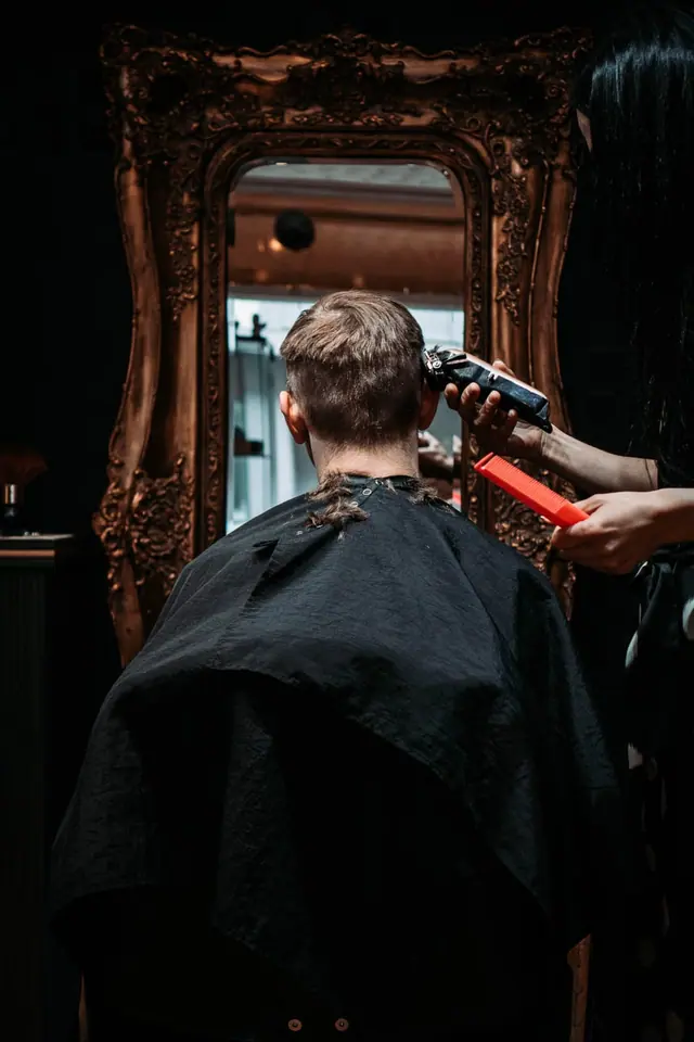 A clipper cut in progress, reflected in a gilded mirror