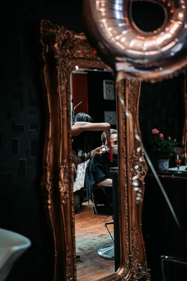 A haircut reflected in a gilded mirror, a copper balloon in front