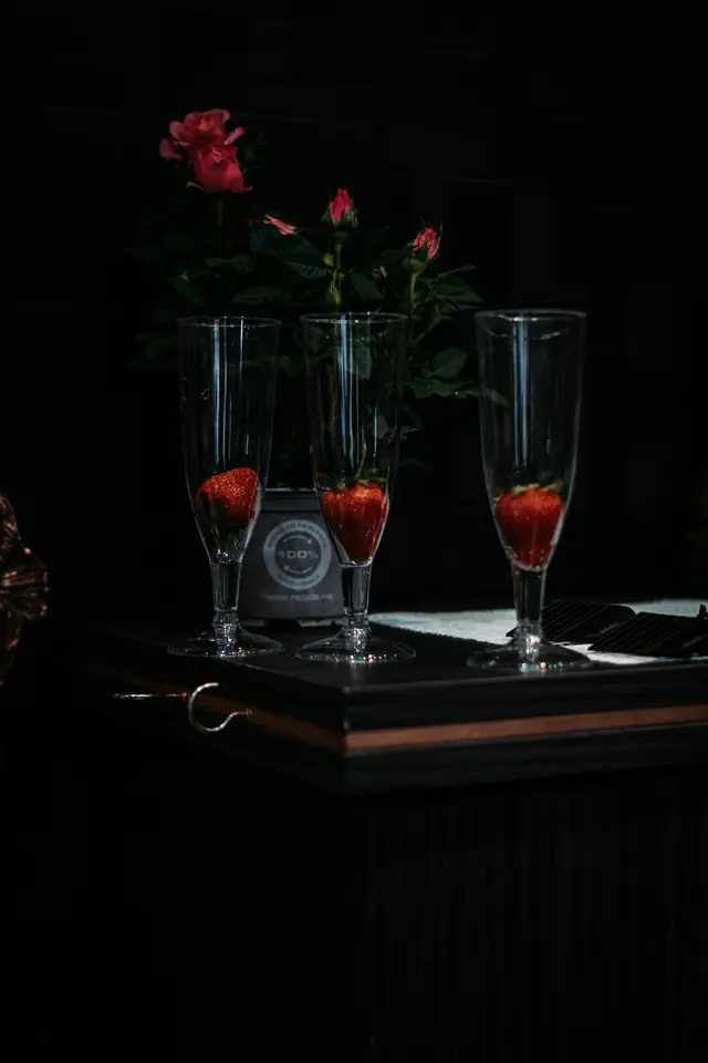 Pink roses and strawberries in champagne flutes on a black counter
