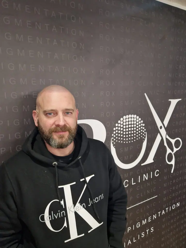 Scalp micropigmentation client in front of the salon wall